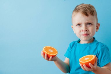 Mavi arka planda elinde portakal tutan küçük çocuk, iyi sağlık kavramı için diyet ve egzersiz yapıyor..