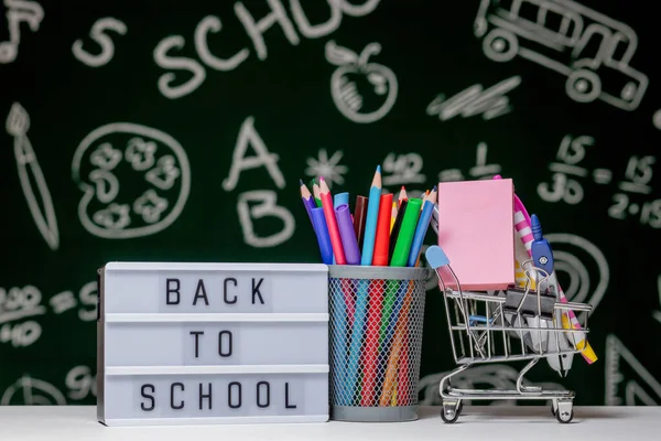 Back to school background with books, pencils and globe on white table on a green blackboard background