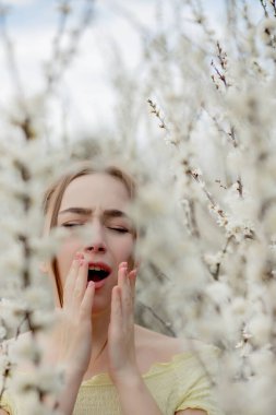 Genç kız sümkürme ve çiçek açan ağacın önünde mendile hapşırma. İnsanları etkileyen mevsimsel alerjik maddeler. Güzel bayanın rhinitis 'i var..
