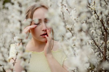 Genç kız sümkürme ve çiçek açan ağacın önünde mendile hapşırma. İnsanları etkileyen mevsimsel alerjik maddeler. Güzel bayanın rhinitis 'i var..