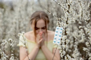 Genç kız sümkürme ve çiçek açan ağacın önünde mendile hapşırma. İnsanları etkileyen mevsimsel alerjik maddeler. Güzel bayanın rhinitis 'i var..