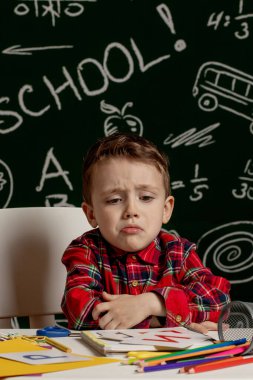 Duygusal okul çocuğu elinde okul malzemeleriyle masada oturuyor. Okulun ilk günü. İlkokuldaki çocuk. Okula dönelim. İlkokuldan bir çocuk