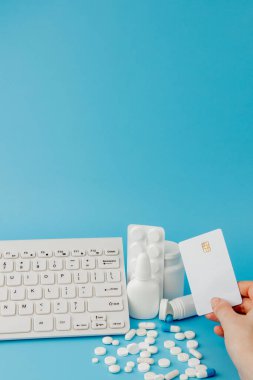 İlaç ve klavyeli alışveriş arabası oyuncağı. Haplar, su toplayan paketler, tıbbi şişeler, termometre, mavi arka planda koruyucu maske. - Evet. Sağlık ve internet alışverişi. Metniniz için en üstteki görünüm.