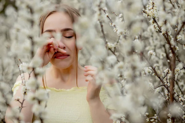 花の木の前で鼻を吹いてティッシュでくしゃみをする若い女の子 季節性アレルゲンが人々に影響を与えます 美しい女性は鼻炎を持っている — ストック写真