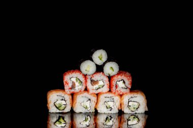 Philadelphia rulosu somon, peynir ve salatalık ile siyah arka planda yansımalı. Suşi Philadelphia.
