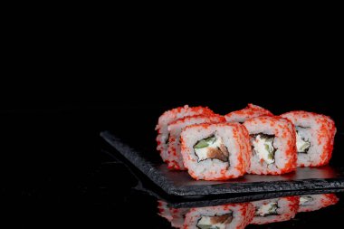 Philadelphia rulosu somon, peynir ve salatalık ile siyah arka planda yansımalı. Suşi Philadelphia.