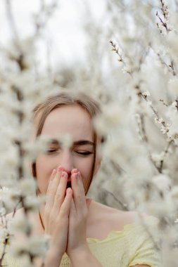 Genç kız sümkürme ve çiçek açan ağacın önünde mendile hapşırma. İnsanları etkileyen mevsimsel alerjik maddeler. Güzel bayanın rhinitis 'i var..
