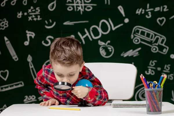 Leuke Slimme Jongen Zit Achter Een Bureau Met Vergrootglas Hand — Stockfoto