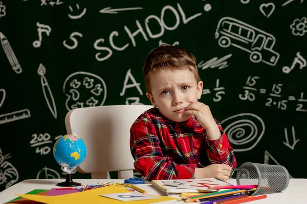 机の上に多くの学校用品を持って座っている感情的な少年 学校の初日だ 小学生の少年 学校に戻る 小学校の子 — ストック写真