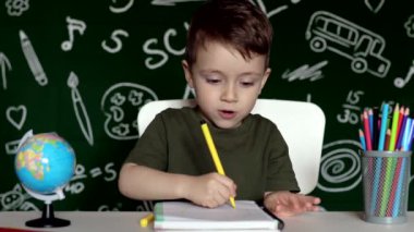 Ev ödevi yapan sevimli çocuk. Masada çizim yapan zeki bir çocuk. Öğrenci çocuk. İlkokul öğrencisi iş yerinde resim çiziyor. Çocuk öğrenmeyi seviyor. Evde eğitim. Okula dönelim. Okuldaki küçük çocuk.