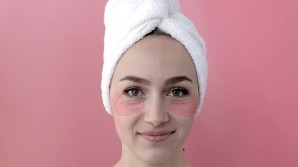 Plesant naken flicka som applicerar kollagen ögonmasker på ansiktet framför en spegel. Porträtt av glad ung kvinna ler och poserar i studion för reklam. — Stockvideo