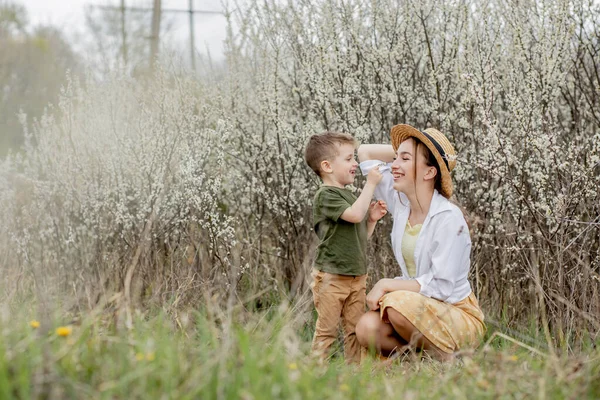 幸せな母親と息子が一緒に楽しんでいます 母は息子を優しく抱きしめる 背景に白い花を咲かせます 母の日 — ストック写真