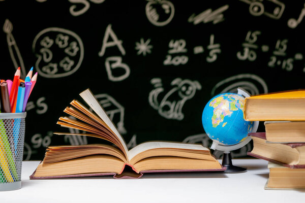 Back to school background with books, pencils and globe on white table on a green blackboard background