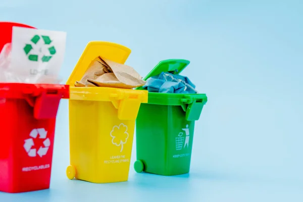 Yellow, green and red recycle bins with recycle symbol on blue background. Keep city tidy, Leaves the recycling symbol. Nature protection concept.