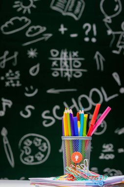 Kırtasiye malzemeleriyle okul geçmişi. Kitap, küre, kalem ve çeşitli ofis malzemeleri yeşil bir karatahta arka planda masanın üzerinde duruyor..