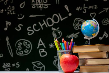 Kitaplar, kalemler ve beyaz masanın üzerindeki elmayla okula geri dön.