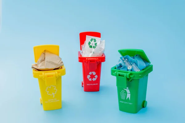 Yellow, green and red recycle bins with recycle symbol on blue background. Keep city tidy, Leaves the recycling symbol. Nature protection concept.