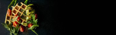 Taze pişmiş Belçika waffle 'ı roka, domates ve siyah bir tabakta avokado. Lezzetli waffle. Kahvaltı konsepti. Sağlıklı kahvaltı..