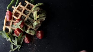 Yemek manzarası hazırlıyorum. Sunum taze pişmiş Belçika waffleları roka, domates ve siyah bir tabakta avokado. Lezzetli waffle. Kahvaltı konsepti