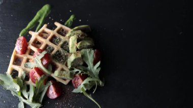Yemek manzarası hazırlıyorum. Sunum taze pişmiş Belçika waffleları roka, domates ve siyah bir tabakta avokado. Lezzetli waffle. Kahvaltı konsepti