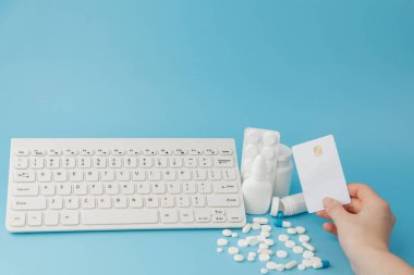 İlaç ve klavyeli alışveriş arabası oyuncağı. Haplar, su toplayan paketler, tıbbi şişeler, termometre, mavi arka planda koruyucu maske. - Evet. Sağlık ve internet alışverişi. Metniniz için en üstteki görünüm.