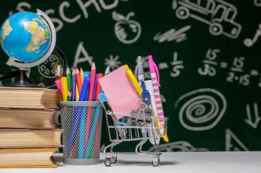 Kitap, kalem ve küre ile okul arka planına yeşil karatahta arka planında beyaz masa üzerinde