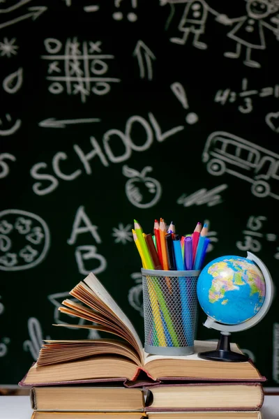 Kitap, kalem ve küre ile okul arka planına yeşil karatahta arka planında beyaz masa üzerinde