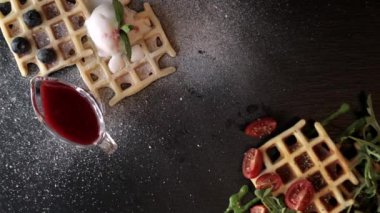 Dondurmalı taze Belçika waffleları, roka, domates, avokado ve waffle, taze yaban mersini ve siyah bir tabakta naneli. Lezzetli waffle. Kahvaltı konsepti. Yemek manzarası hazırlıyorum..
