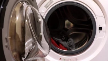 Bir kadın çamaşır yıkar. Bir kadın çamaşır makinesine çamaşır koyar. Ev işleri.