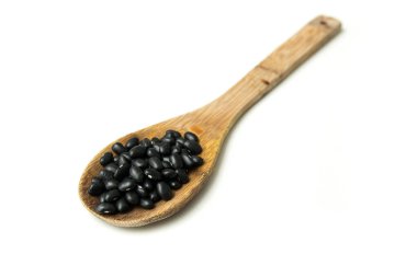 Beyaz grupta izole edilmiş tahta bir kaşıkta çiğ Brezilya Siyah Fasulyesi yığını.