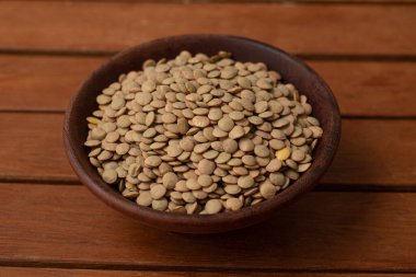 Tahta bir masanın üzerinde bir kâse dolusu çiğ mercimek.