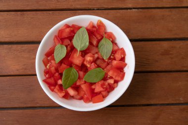 Tahta bir masanın üzerinde fesleğenle doğranmış veya doğranmış domatesler.