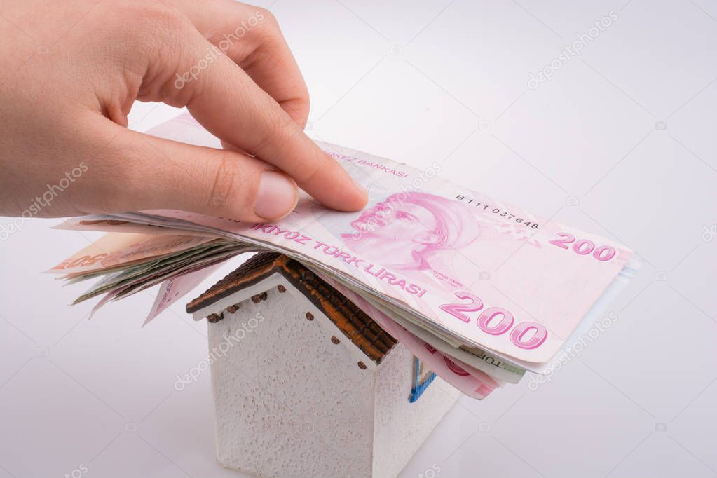 Hand holding Turkish Lira banknotes on the roof of a model house