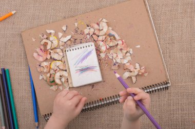 Elinde kalem çöpü olan sarmal defterlerin üzerinde renkli bir kalem tutuyordu.