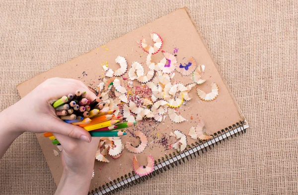 Bir defter kalem talaş ile üzerinde renkli kalemler tutan el