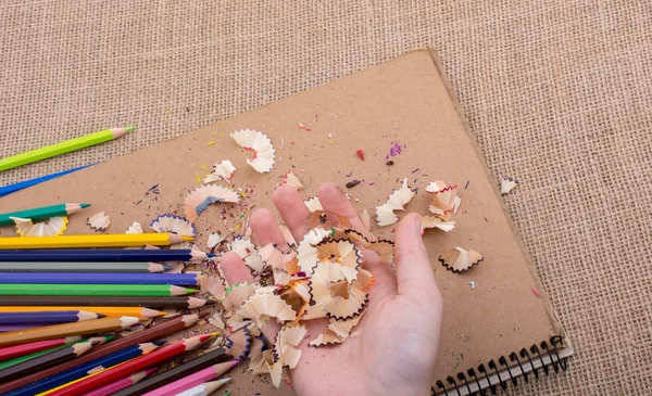 Elindeki renkli kalem talaşları bir deftere.