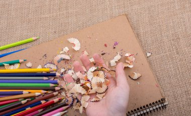 Elindeki renkli kalem talaşları bir deftere.