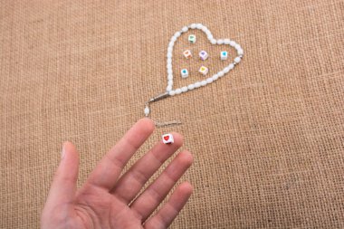 Elinde kalp şeklinde bir nesne, tuvalde dua eden boncuklarla.