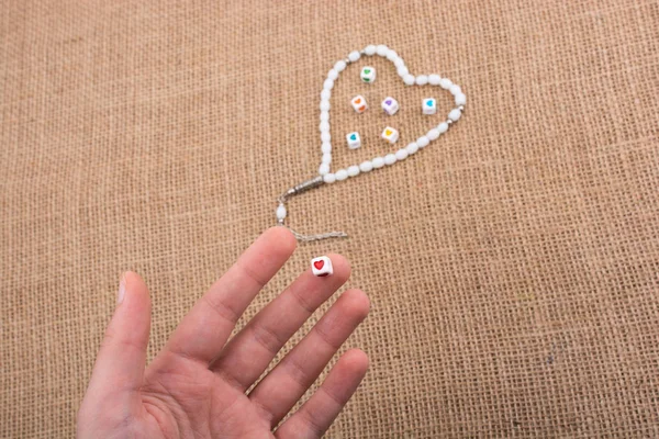 Elinde kalp şeklinde bir nesne, tuvalde dua eden boncuklarla.