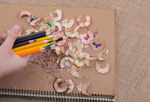 Bir defter kalem talaş ile üzerinde renkli kalemler tutan el