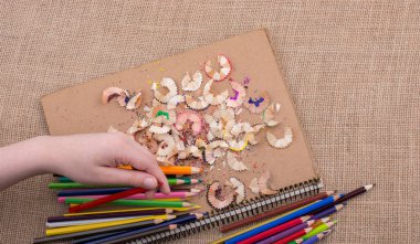 Bir defter kalem talaş ile üzerinde renkli kalemler tutan el