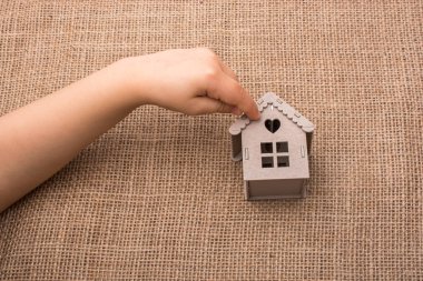 Çocuk keten bir tuvalde model bir evi tutuyor.