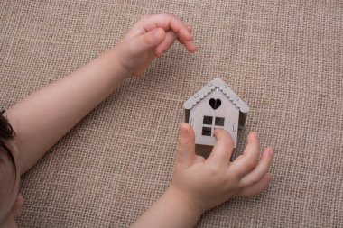Çocuk keten bir tuvalde model bir evi tutuyor.