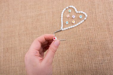 Elinde kalp şeklinde bir nesne, tuvalde dua eden boncuklarla.