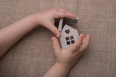 Çocuk keten bir tuvalde model bir evi tutuyor.