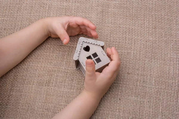 Çocuk keten bir tuvalde model bir evi tutuyor.