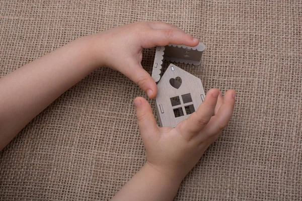 Çocuk keten bir tuvalde model bir evi tutuyor.