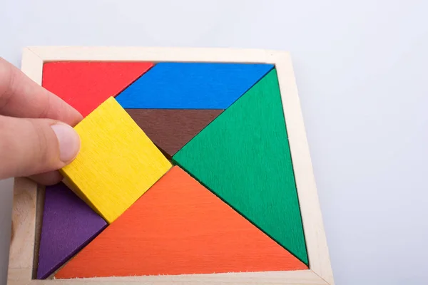 Mão segurando uma peça em falta em um quebra-cabeça tangram — Fotografia de Stock