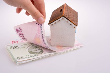 Beyaz arka planda, model evin yanında Türk Lirası banknotları el ele tutuşuyor