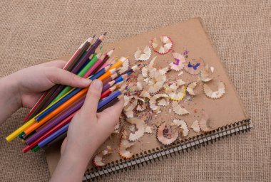 Bir defter kalem talaş ile üzerinde renkli kalemler tutan el